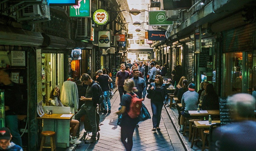 A colourful Melbourne laneway lined with café tables, street art and hanging string lights.