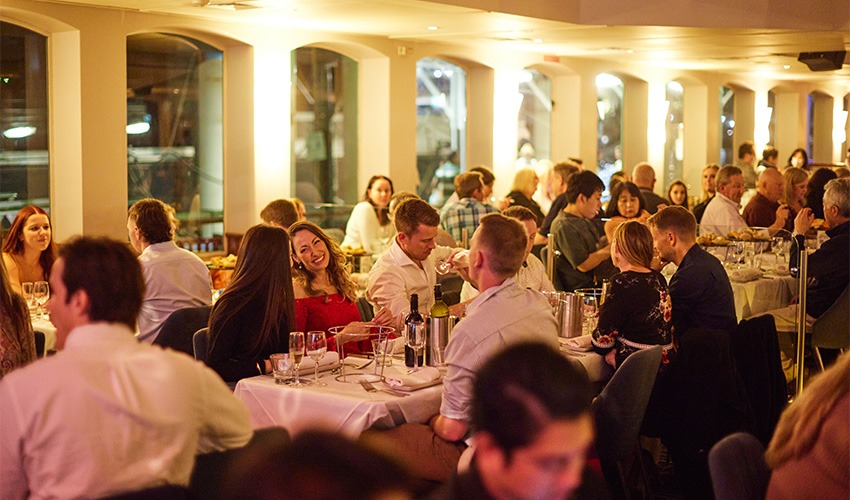 Dinner cruise guests seated at candlelit tables aboard the Sydney Showboat as it passes the Harbour Bridge.