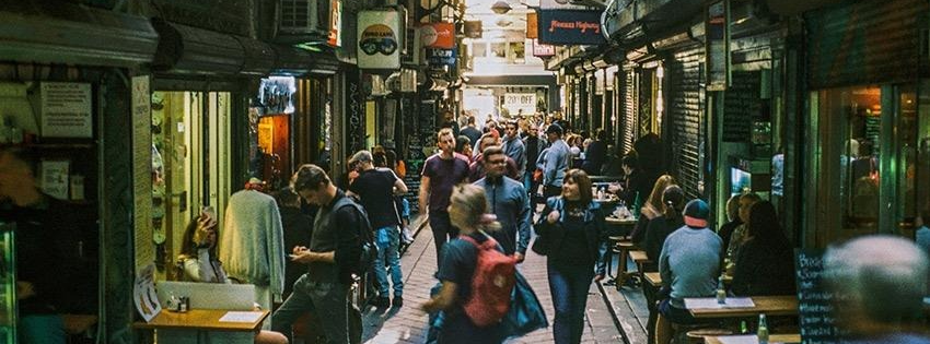 A colourful Melbourne laneway lined with café tables, street art and hanging string lights.